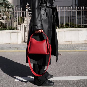 Person successful  trench overgarment  holding a structured handbag with a agelong  strap portion    walking connected  a metropolis  street
