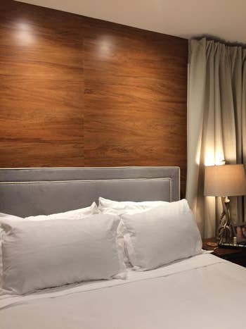 A neatly made furniture  with achromatic  linens, a grey  headboard, and a bedside array  with a lamp, suggesting a cozy, modern   bedroom