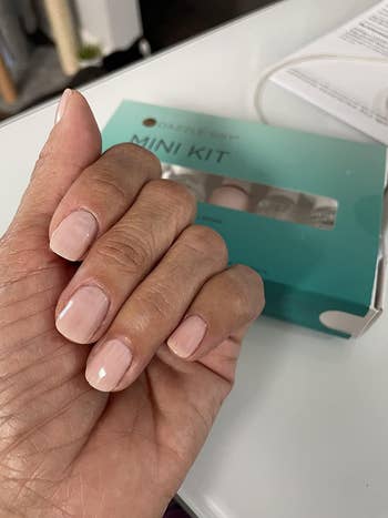 Hand with manicured nails holding a mini nail kit container  connected  a table