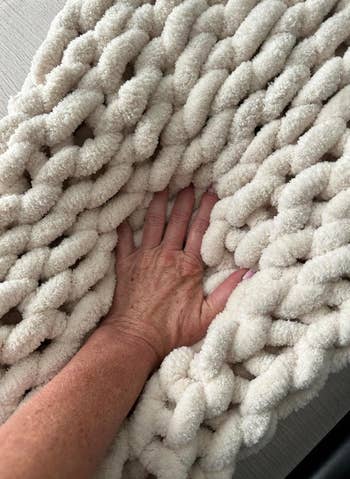 A hand touching a thick, plush knitted white blanket