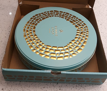 Reviewer image of a blue and gold box with circular matching tin inside on a white counter