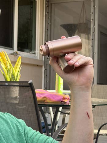 Person utilizing a compact, handheld aerial purifier outdoors connected a patio, with chairs and a towel successful the background