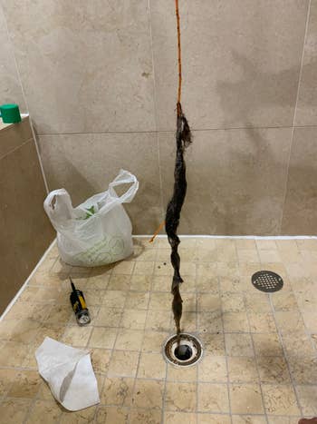 The drain snake coming out of a shower drain with a bunch of hair on it 