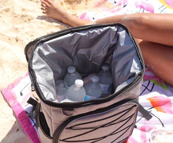 Reviewer shows open white cooler of water bottles while sitting on a beach blanket 