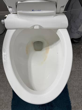 Toilet bowl with mineral stains, viewed from above, placed on a textured mat