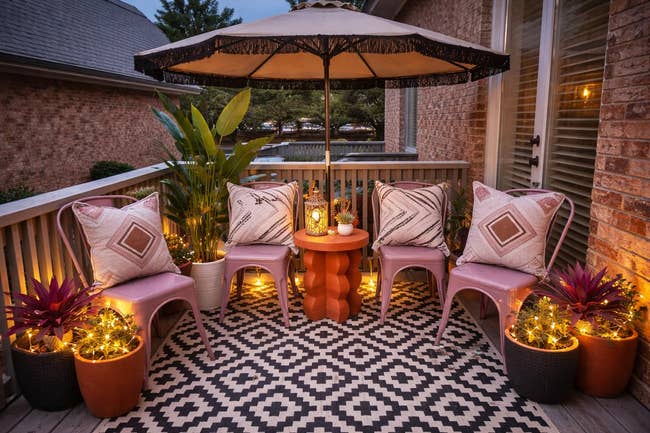 Cozy patio setup with patterned rug, chairs, table, potted plants, and ambient lighting nether  a ample  umbrella