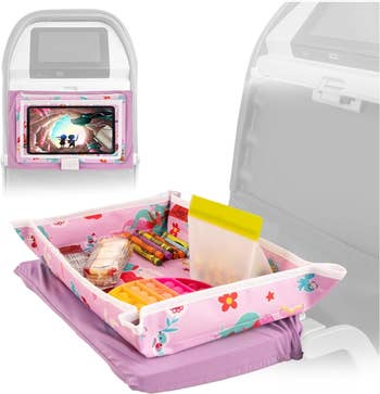 A pink unicorn patterned tray with raised edges sitting on a plane tray table holding snacks 