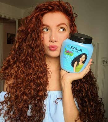 A model with curly red hair holding the product