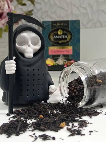 Toy grim reaper next to spilled tea leaves from a jar, with Amatea Equilibrio Day tea package in the background