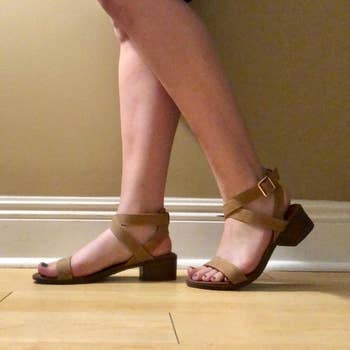 Person wearing strappy sandals with block heels, standing on a wooden floor