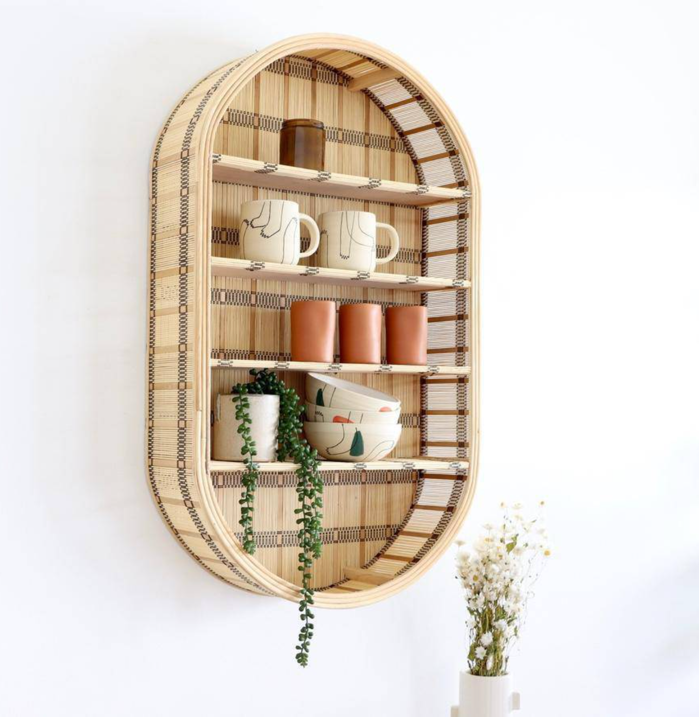 Oval rattan with four shelves wall-mounted with mugs and plants 