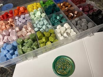 the wax seal stamp kit with all the colored waxes next to a wax seal in green