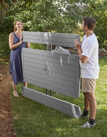 two models holding up the folded picnic table and benches, which are completely flat