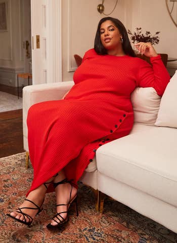 a model in a red knit dress lounging on a couch