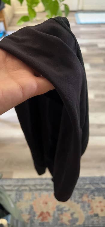 A hand holding a black shirt, showcasing its fabric and texture. No recognizable persons in the image