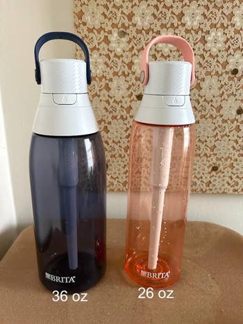 Two Brita water bottles on a table, one 36 oz in navy and one 26 oz in pink, both with built-in straws