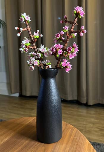 A simple black vase on a wooden table holding the lego cherry blossoms