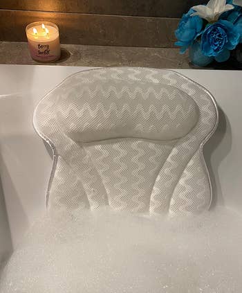 reviewer photo of the bath pillow in a bubble bath with a lit candle behind it