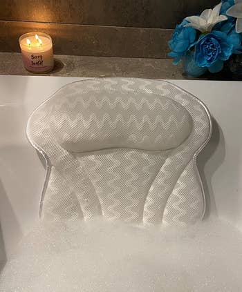 reviewer photo of the bath pillow in a bubble bath with a lit candle behind it