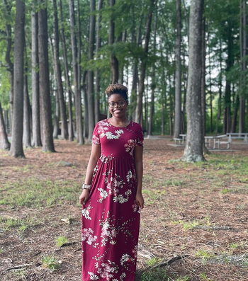 Individual in a floral dress standing in a wooded pickle