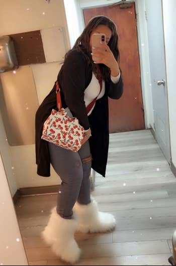 Person successful a reflector selfie wearing a agelong cardigan, jeans, achromatic fluffy boots, and a patterned handbag