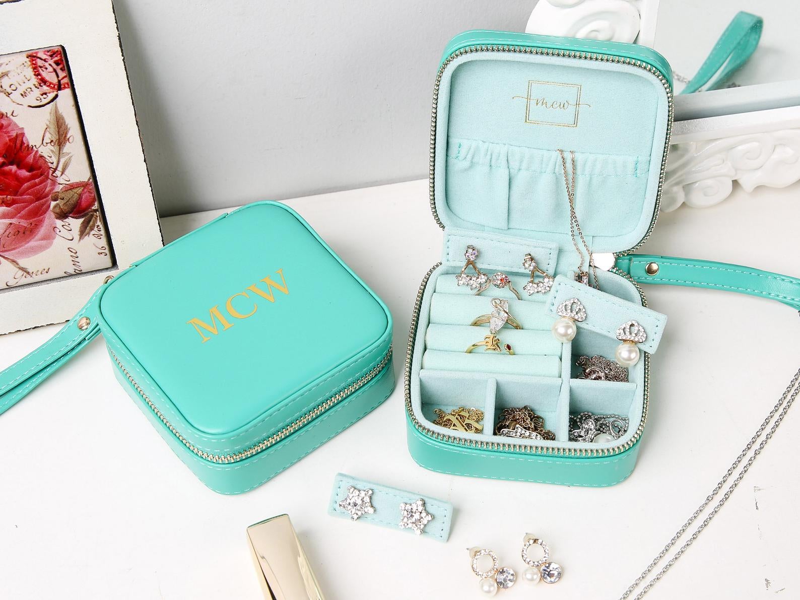 Small blue squared-shaped zippered pouch with wrist strap that opens up to soft compartments for jewelry to store in