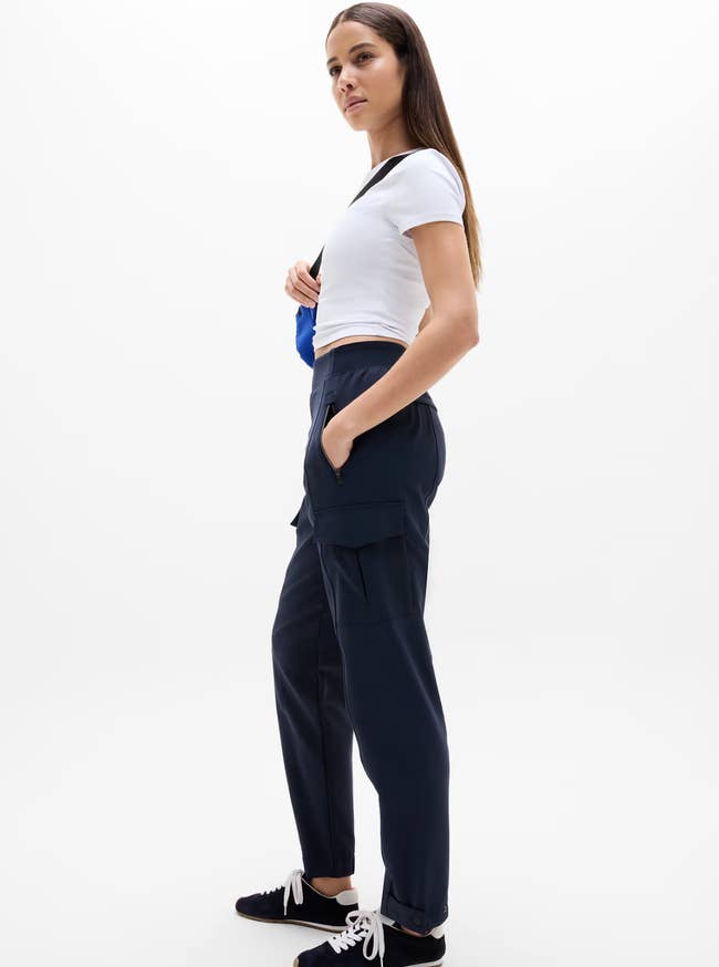 model wearing a achromatic tee, navy cargo pants, and sneakers, holding a bluish bag. Fashion-forward and casual benignant perfect for shopping