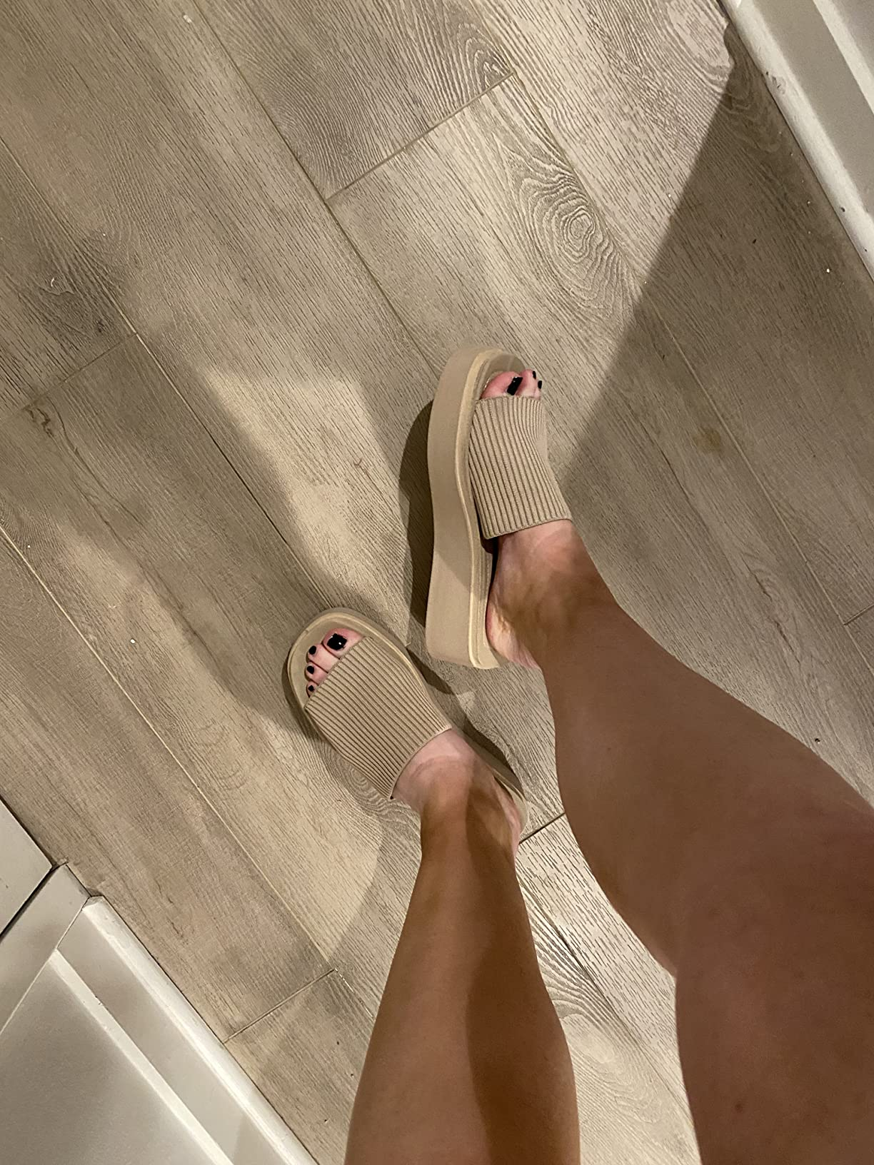 Person wearing beige descent  sandals with a textured strap and elevated sole, lasting  connected  a woody  floor