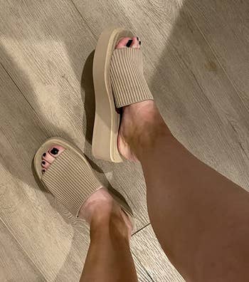 Person wearing beige descent sandals with a textured strap and elevated sole, lasting connected a woody floor
