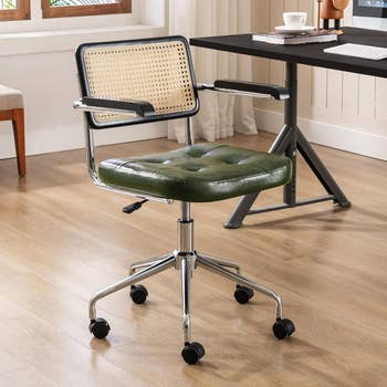 An office chair with green cushioned seat and wicker backrest, on wheels, in an indoor setting