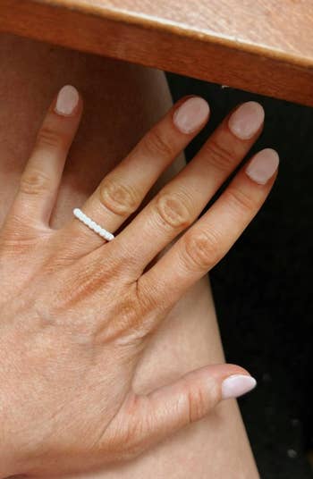 A manus  with short, shiny nails wearing a elemental  beaded ring, resting connected  a person's leg, suggesting a minimalist manner  accessory style