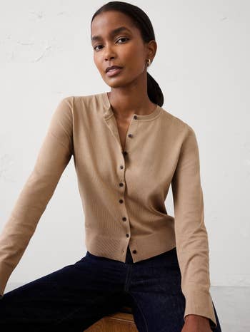 model wearing a button-up cardigan and jeans, posing against a neutral background