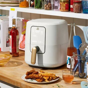 A modern air fryer on a kitchen counter with fried food and utensils nearby, promoting convenient cooking solutions
