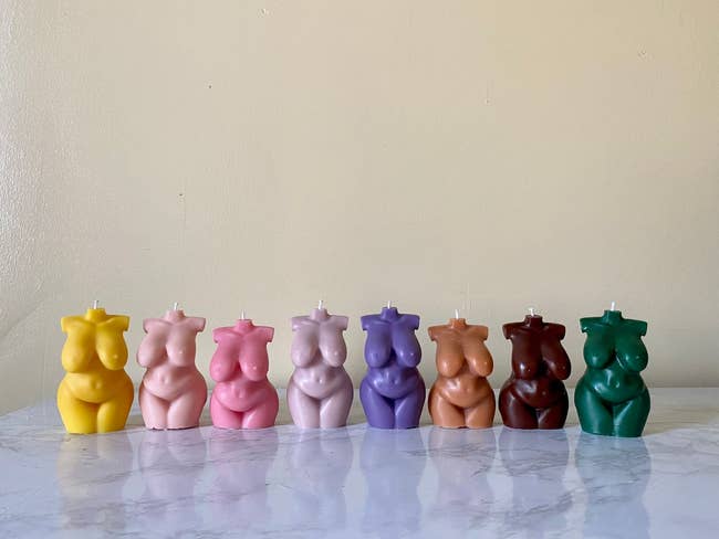 Candles shaped similar  pistillate  torsos successful  assorted  colors are lined up   connected  a marble surface