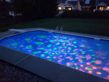 Outdoor excavation  with colorful lights successful  the h2o  astatine  night, surrounded by a grassy gait   and houses successful  the background