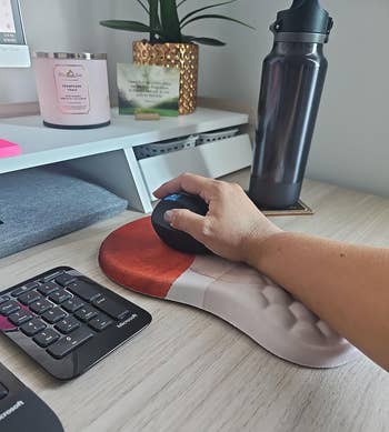 Person's hand using an ergonomic mouse on a desk with office supplies