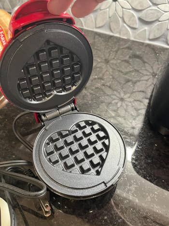 Reviewer opening a heart-shaped waffle maker on a kitchen counter