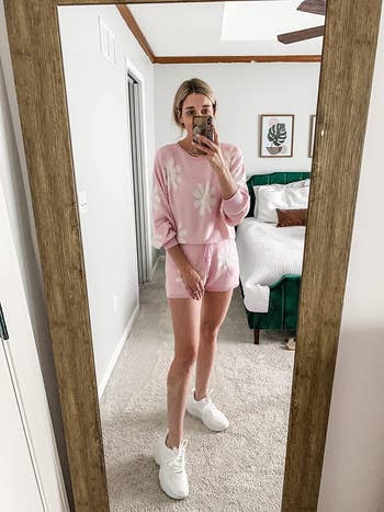 Person in a casual pink floral loungewear set taking a mirror selfie in a bedroom