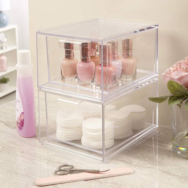 Two clear pullout squared shaped storage drawers with cosmetics in them stacked on top of each other 