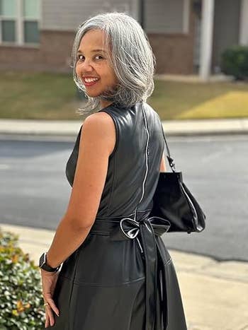 Person outdoors wearing a sleeveless, belted leather dress, smiling portion looking back