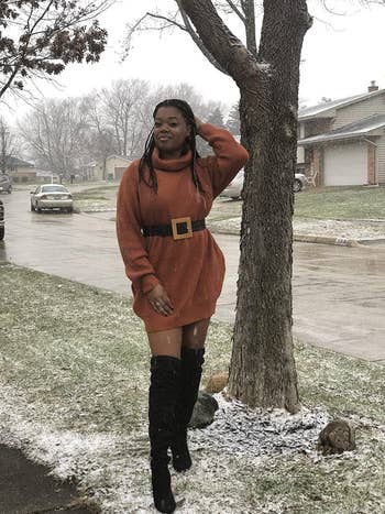Woman successful  a belted turtleneck formal  and knee-high boots walking connected  a snowy street, touching her hair