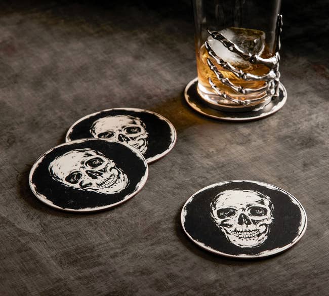 the four skull painted coasters next to a skeleton themed whiskey glass