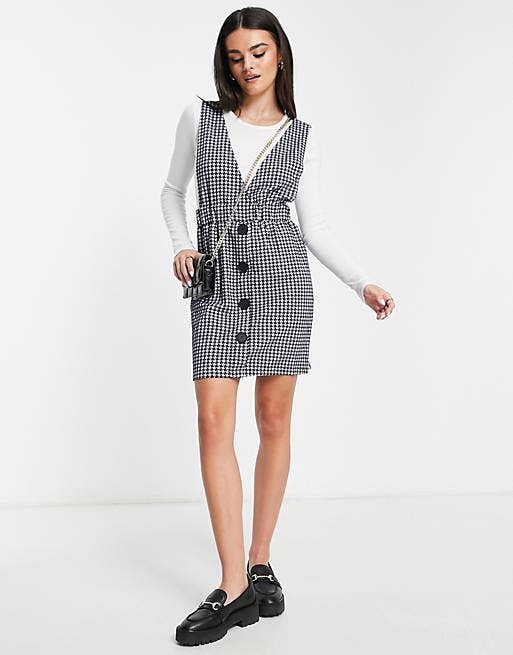 model in black and white v neck pinafore dress with buttons and above the knee length over long sleeve tee