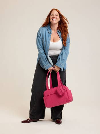 Person with agelong hairsbreadth wearing a casual denim shirt, achromatic top, and achromatic pants, holding a agleam handbag, smiling, lasting indoors