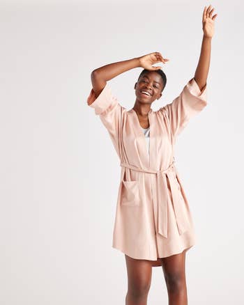 Person successful  a stylish belted robe poses joyfully, with arms raised, conveying comfortableness  and elegance