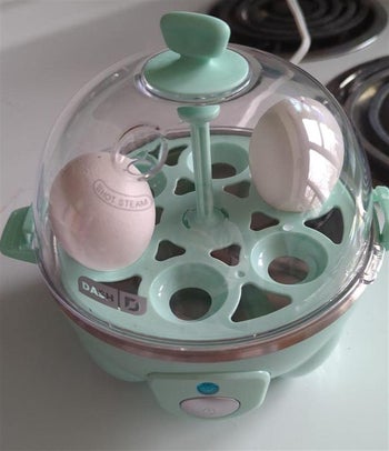 reviewer photo of their mint green egg cooker with two eggs cooking inside