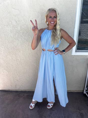 Person in a sleeveless cut-out dress and sandals poses with a peace sign