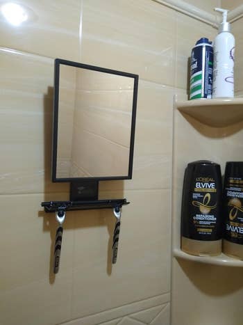 Mirror mounted on bathroom tile with shelf holding toiletries and razors