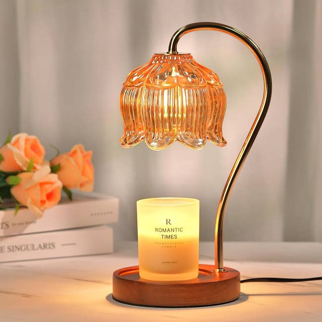 A gold-stemmed lamp with a flower-shaped bulb shining light down on a warmed candle 