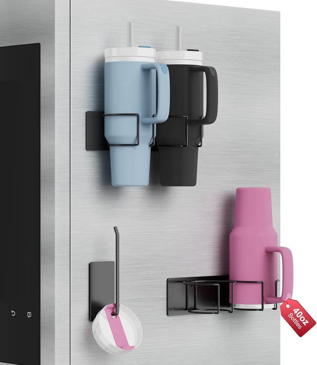 Tumbler retention holders attached to a fridge, holding ample mugs with straws and pinkish thermos